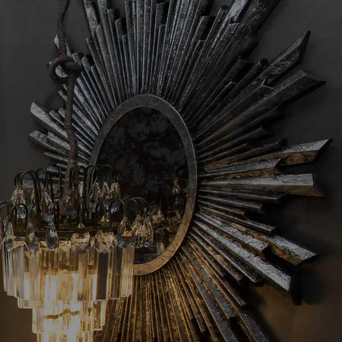 Detail of a sunburst mirror in weathered dark timber, with a crystal chandelier hanging across it
