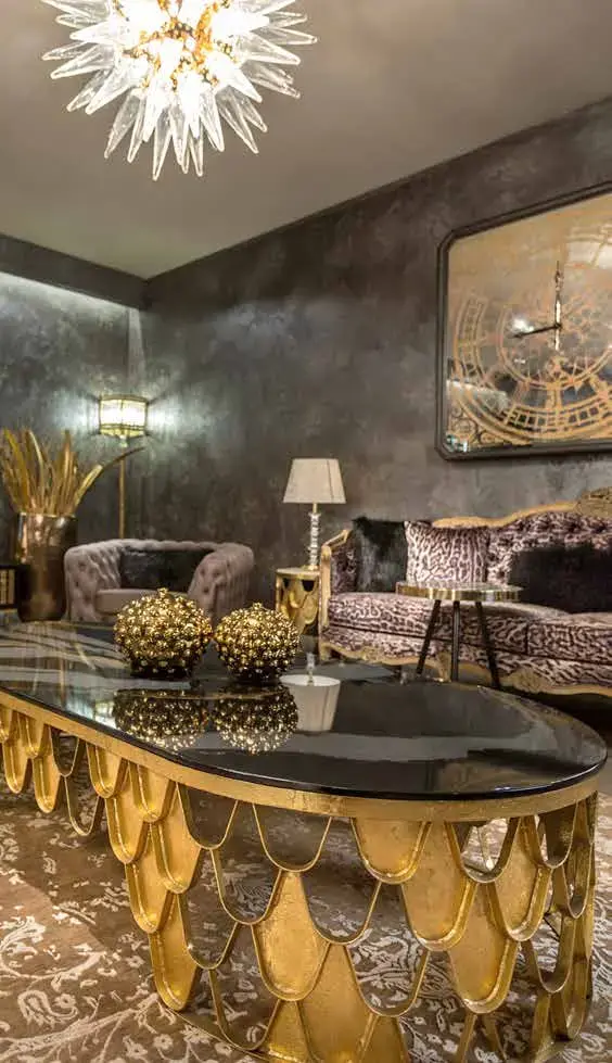 Scalloped gold oval coffee table beneath a crystal chandelier, with a patterned sofa behind
