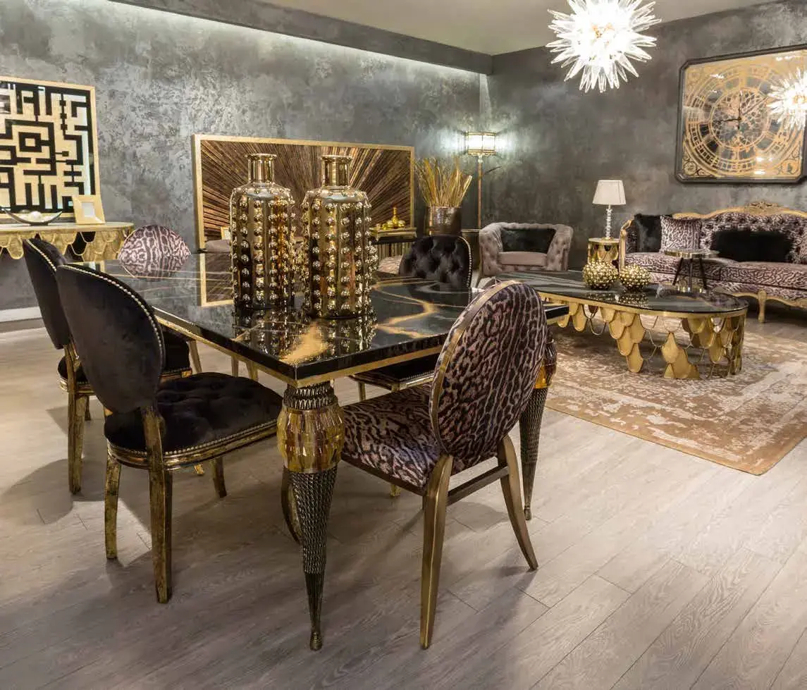 Dining room with black and leopard-print chairs around a glass table, set with gold studded vases below a gilded wall panel