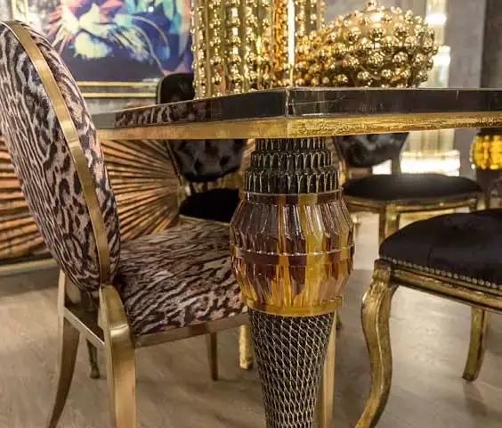 Close view of a turned gold table leg between leopard-print and black dining chairs