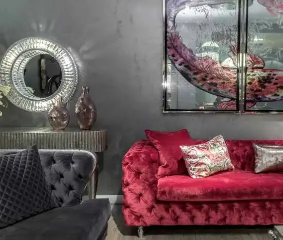 Crimson buttoned sofa and a charcoal velvet sofa, with a silver sunburst mirror on the wall between them