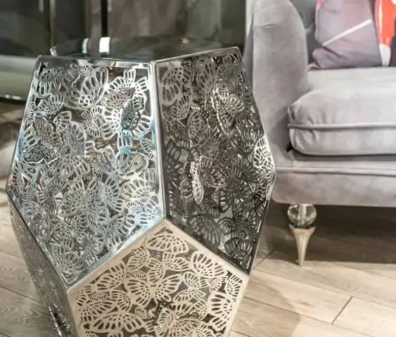 Faceted silver side table with butterfly-pierced panels, standing beside a grey velvet sofa