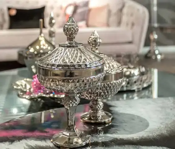 Ornate silver lidded bowl on a footed stem, reflected in a glass table top